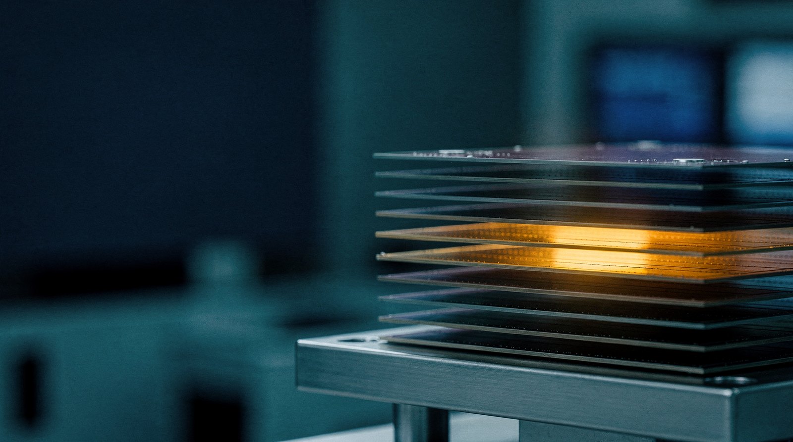 A stack of thin memory dies viewed edge-on under magnification, one layer in the stack lit warm gold
