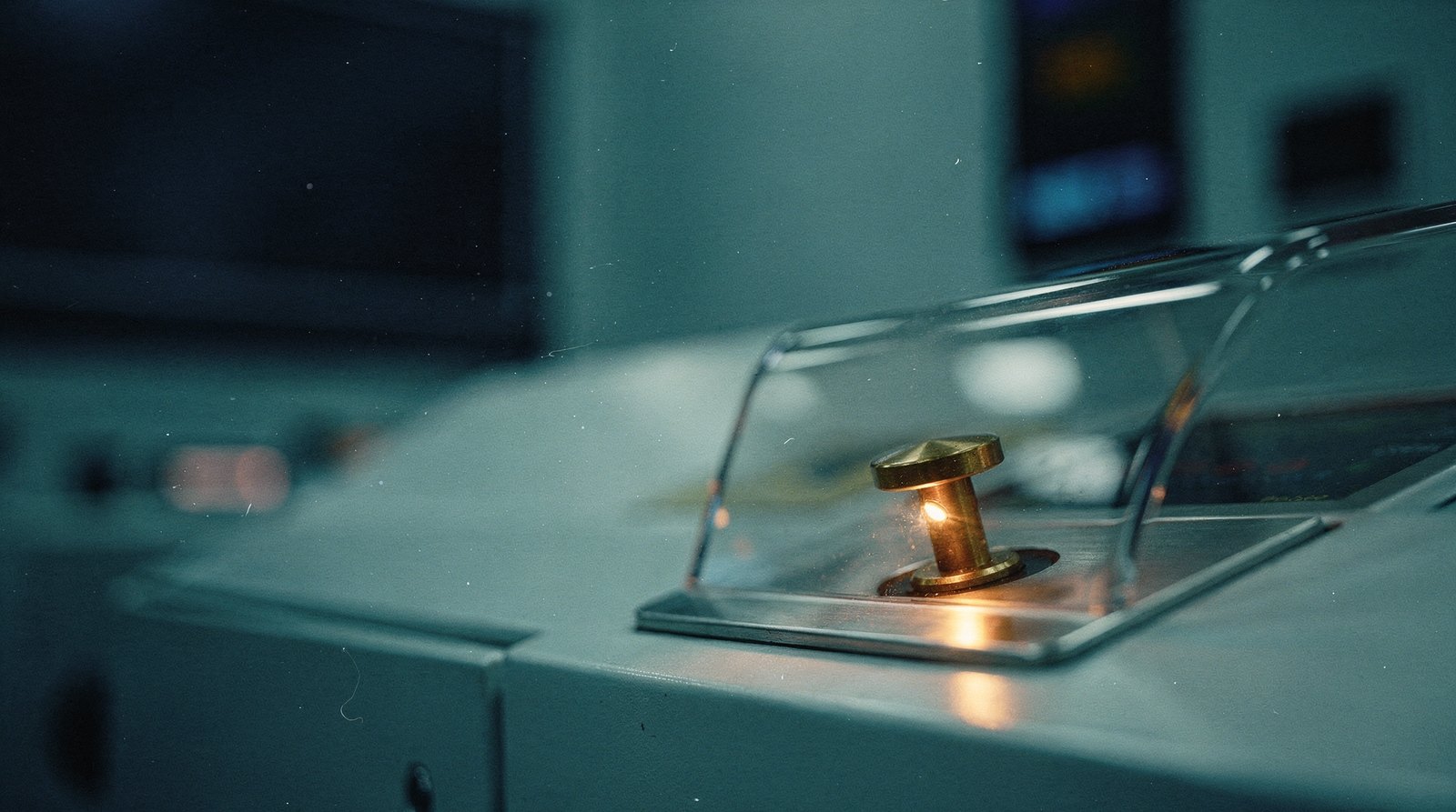 A machine's physical stop lever under a clear safety cover, the lever lit warm gold